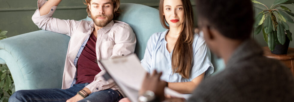 Young serious couple visiting a psychologist sitting on the comfortable couch during psychological session in the green office