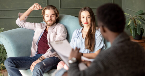 Young serious couple visiting a psychologist sitting on the comfortable couch during psychological session in the green office